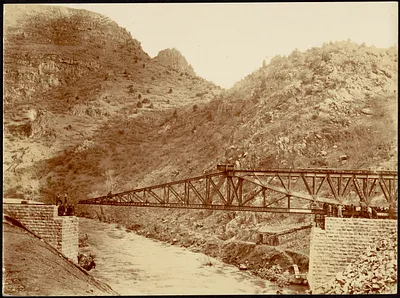 Construction of steel bridge over a river with men standing on stone anchorage
