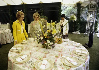 First Lady Betty Ford, Social Secretary Maria Downs, and an Unidentified Woman Examining Table Settings and Decorations in the Tent on the South Lawn of the White House during Preparations for a State Dinner Honoring Queen Elizabeth II and Prince Philip of Great Britain