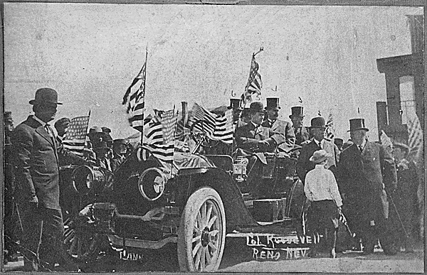 "Col. Roosevelt, Reno, Nev." Campaigning from an open touring car decorated with American flags, ca. 1912. Theodore Roosevelt is No. 3; his chauffeur is at the crank