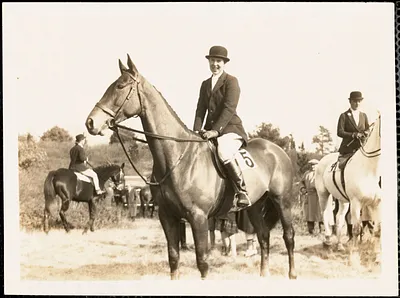 Woman in formal riding clothes astride a horse in a field setting