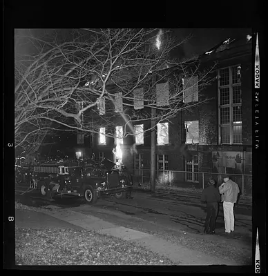 Fire truck on the side of road outside a building on fire