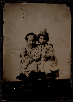 Possibly Isabel and Helen Stevens, sitting in chair holding dolls