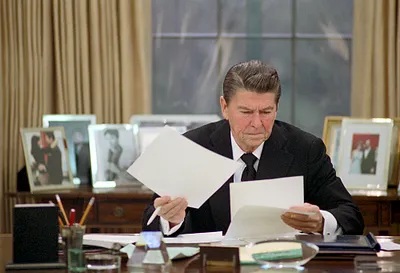 President Ronald Reagan sitting at his desk and being filmed by NBC working in the Oval Office for the program "A Day in the Life of the President"