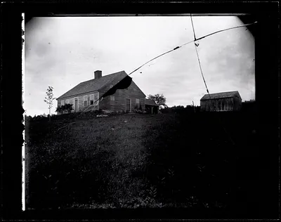 Wood farmhouse on a hill with large central chimney and twelve-over-twelve double-hung windows
