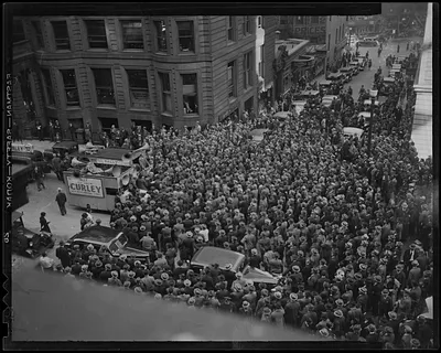 Crowd of people in the streets as cars make their way down