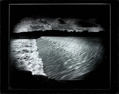 Time-lapse image of water flowing over the dam, with Holyoke skyline in the background